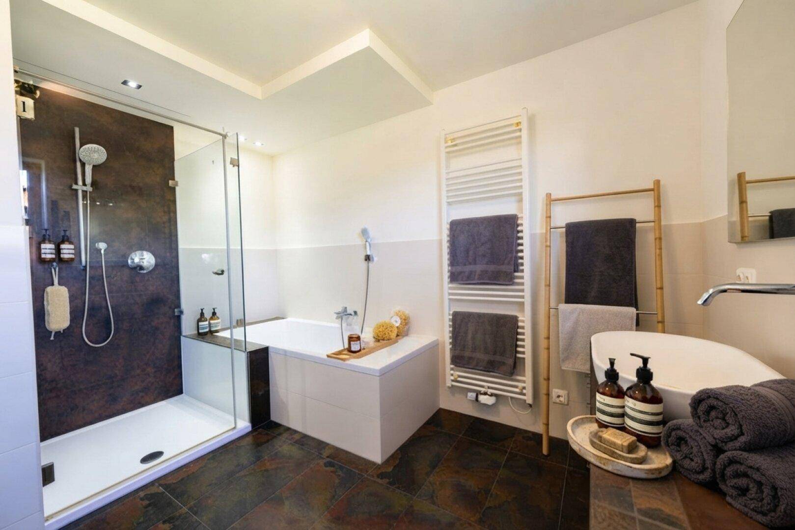 Modernes Badezimmer mit begehbarer Dusche, Badewanne und dunklen Fliesen.