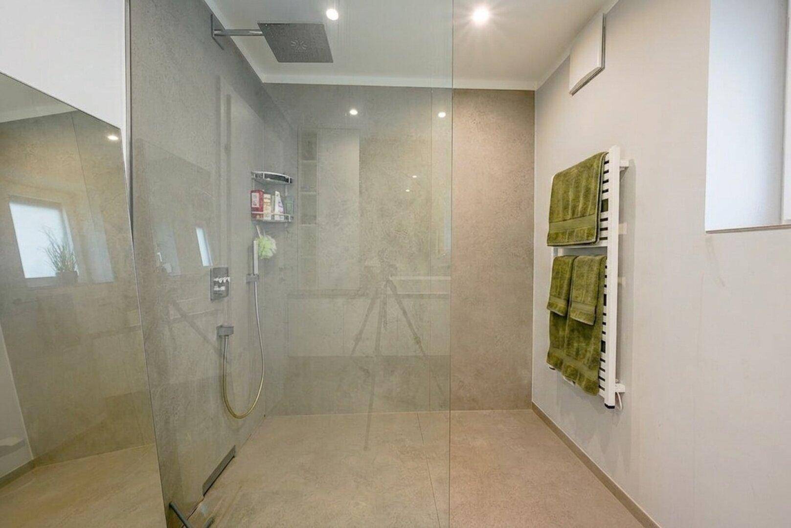 Modernes Badezimmer mit großer begehbarer Dusche, Glaswand und beheiztem Handtuchhalter.