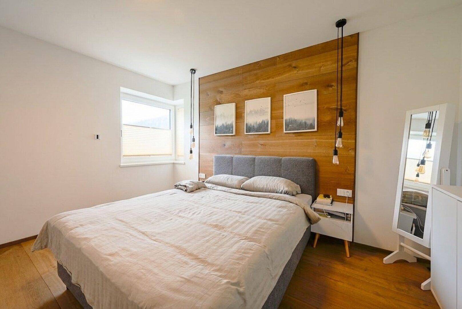 Gemütliches Schlafzimmer mit Holzwandakzent, Doppelbett und modernen Hängelampen.