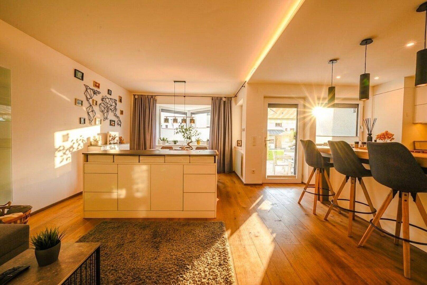 Heller offener Wohnbereich mit Holzboden, Kücheninsel und viel natürlichem Licht durch große Fenster.