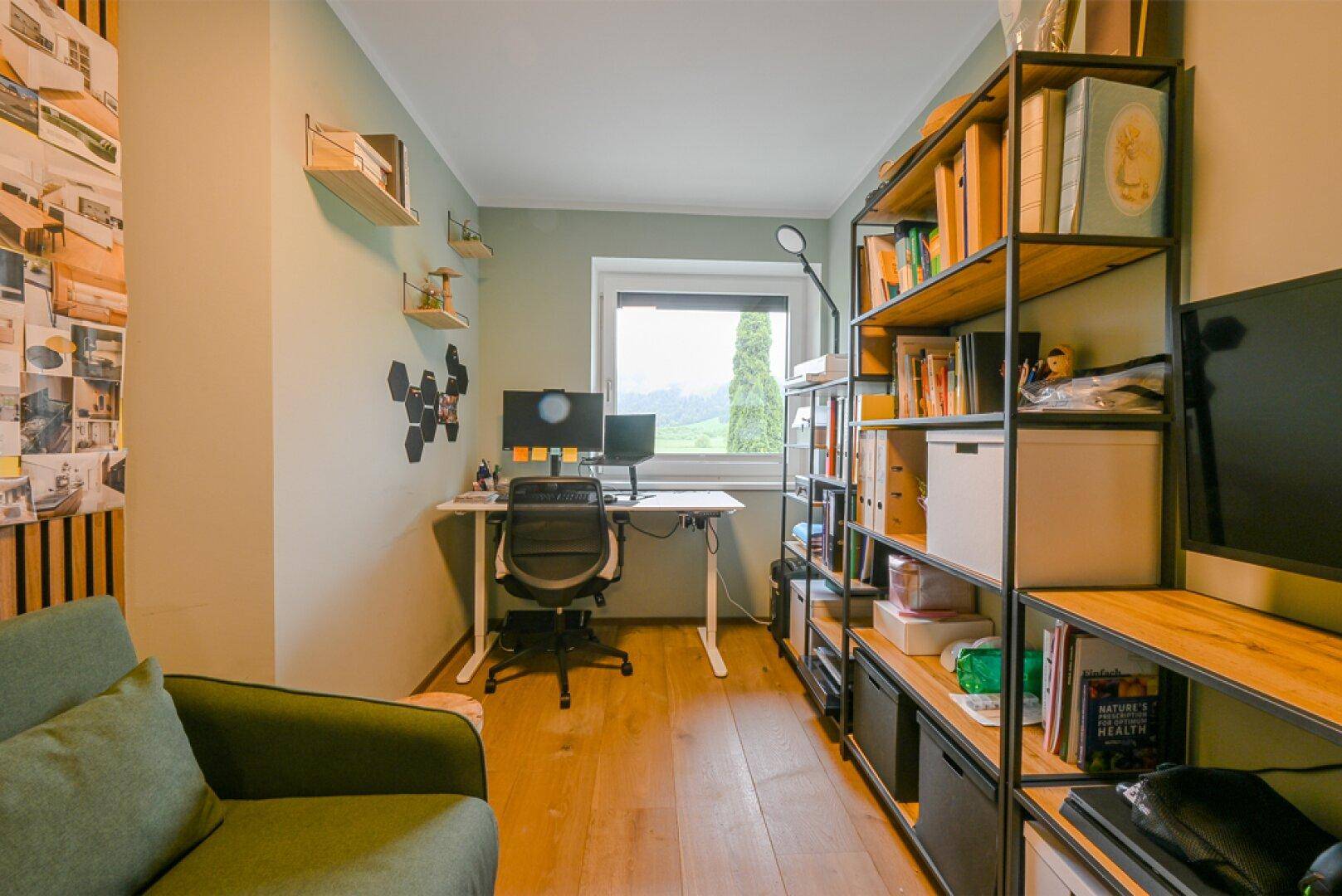 Funktionales Heimbüro mit Schreibtisch, Bücherregal und Blick ins Grüne durch das Fenster.
