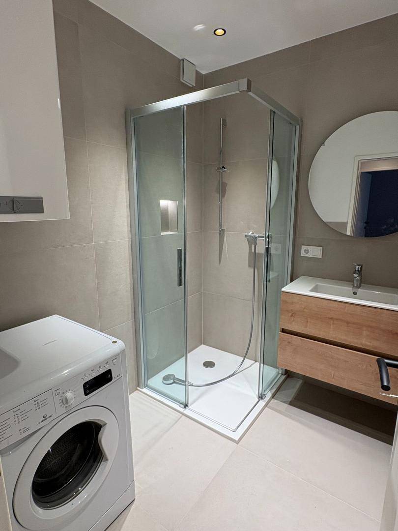 Modernes Badezimmer mit Duschkabine, Waschbeckenunterschrank und integrierter Waschmaschine.