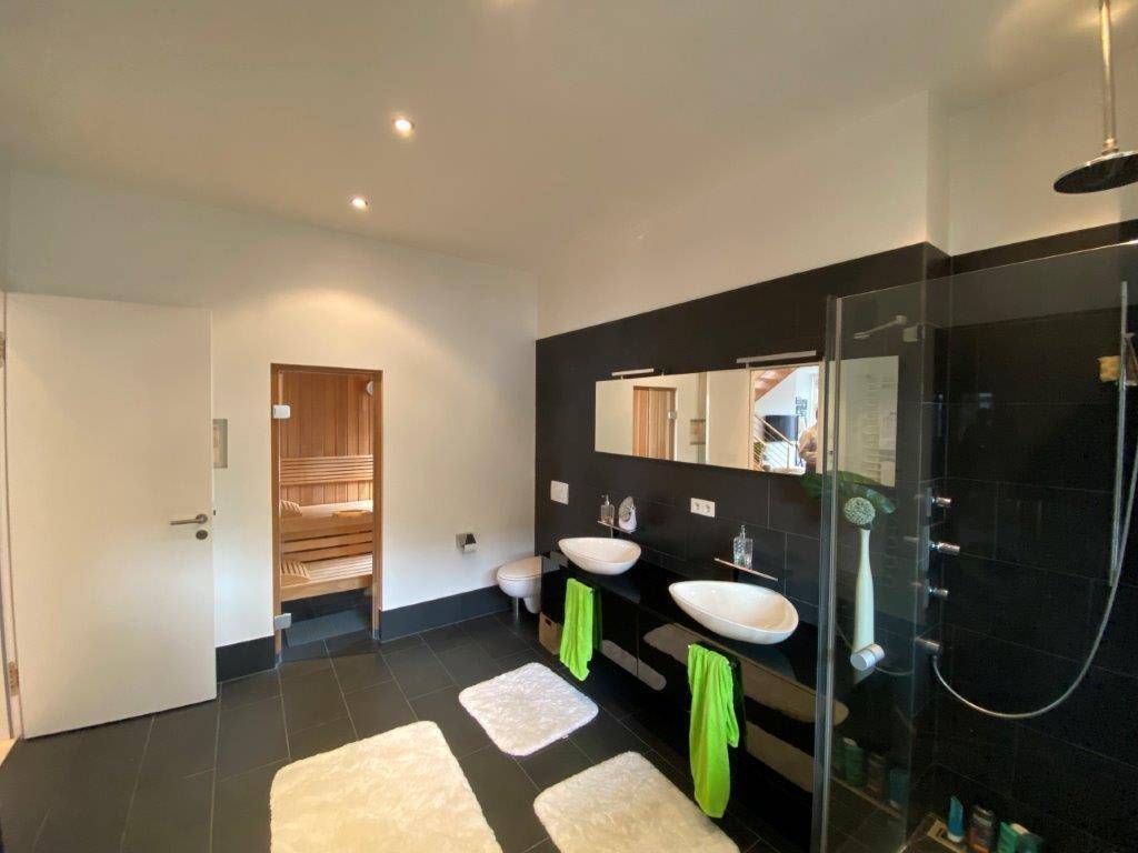 Modernes Badezimmer mit Doppelwaschbecken, großer Dusche und integrierter Sauna für Wellness.