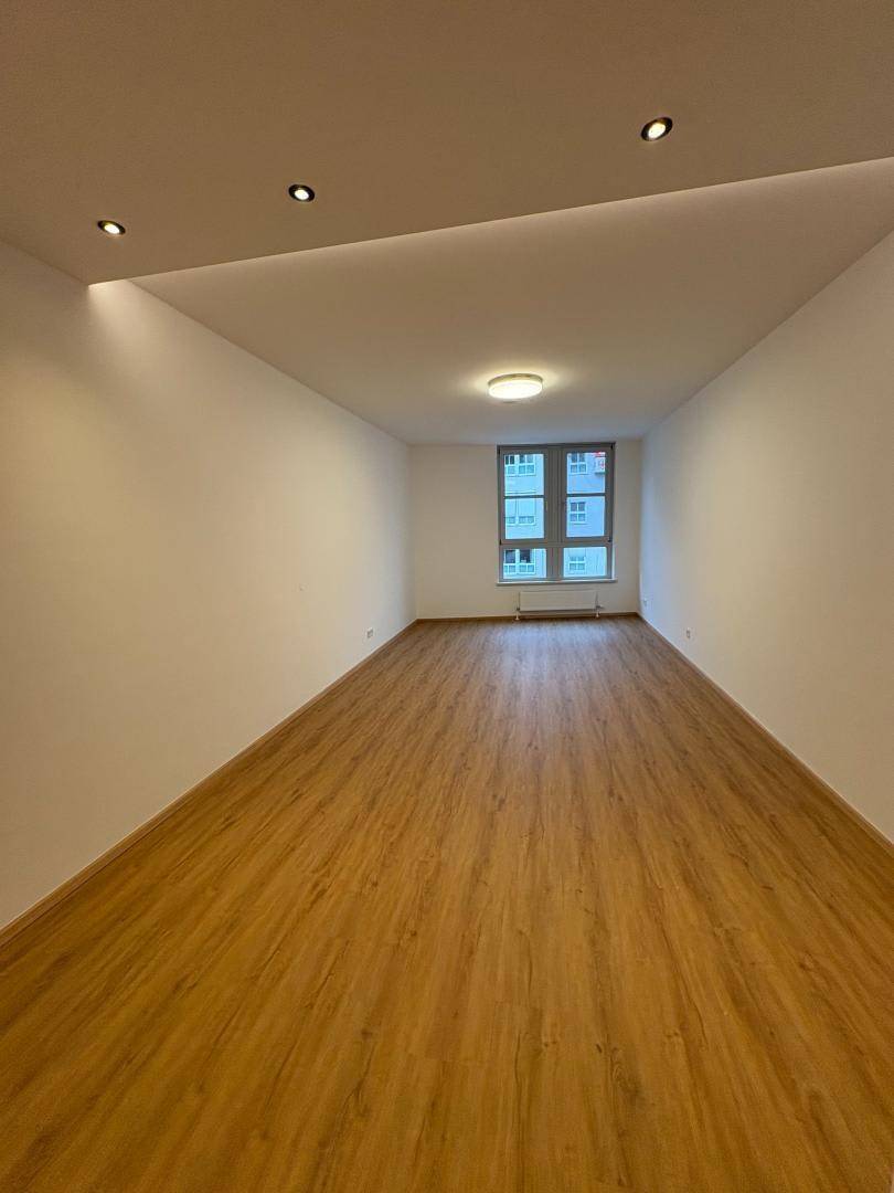 Langer, heller Raum mit Laminatboden, weißen Wänden und einem Fenster am Ende des Raumes.