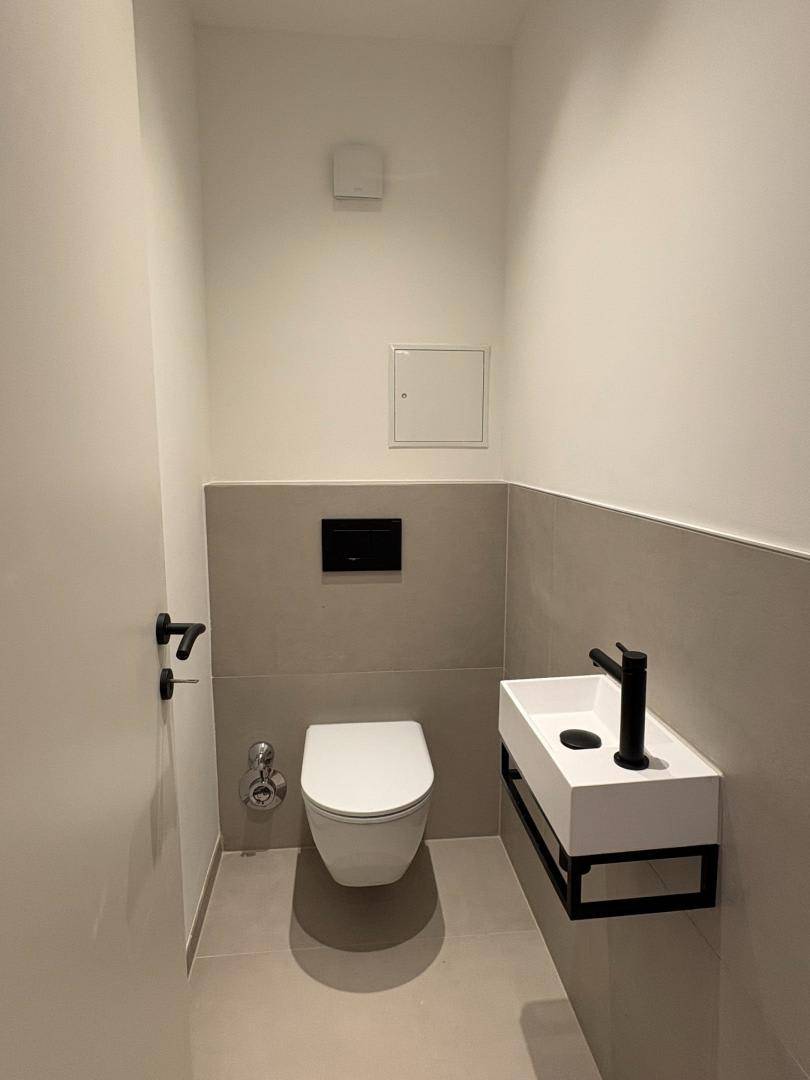Modernes Gäste-WC mit wandhängender Toilette, stilvollem Waschbecken und grauen Fliesen.