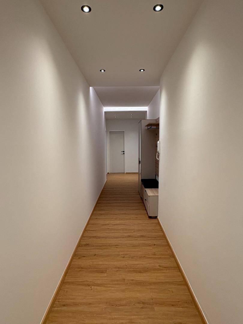 Langer, heller Flur mit modernem Laminatboden und integrierter Deckenbeleuchtung.