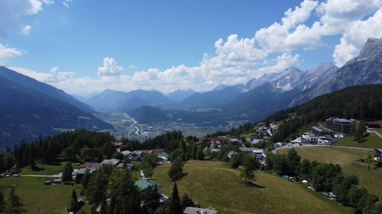 Panoramablick über ein weites Tal mit einer Stadt, einem Fluss und majestätischen Bergen im Hintergrund.