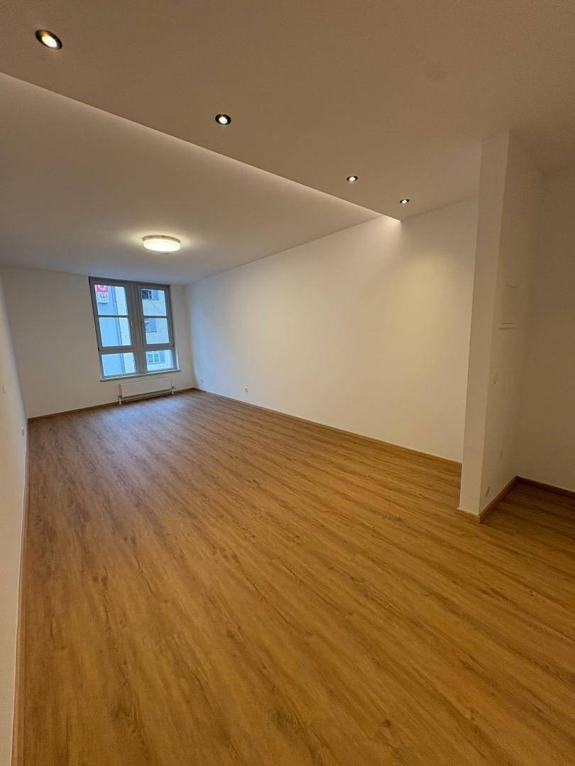 Heller, geräumiger Raum mit Laminatboden, weißen Wänden und einem großen Fenster.