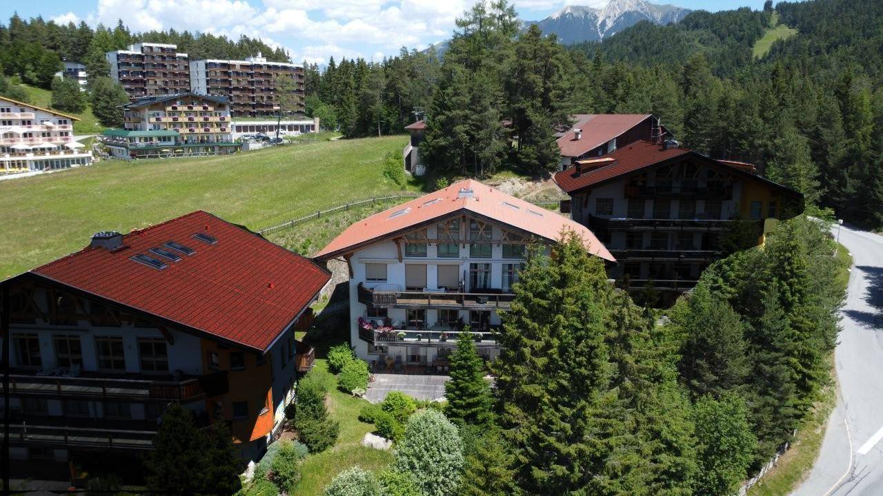 Luftaufnahme von traditionellen Gebäuden mit roten Dächern in einer bergigen, bewaldeten Landschaft.