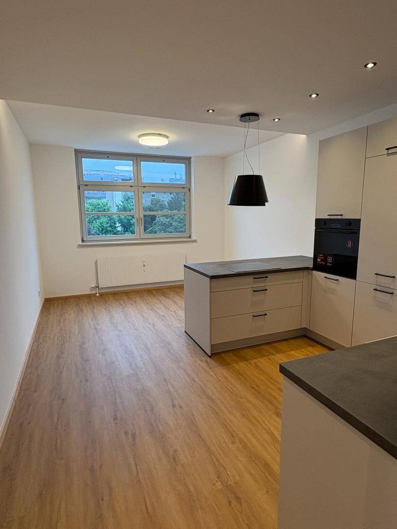 Offener Wohnbereich mit integrierter Küchenzeile und Blick auf ein großes Fenster.
