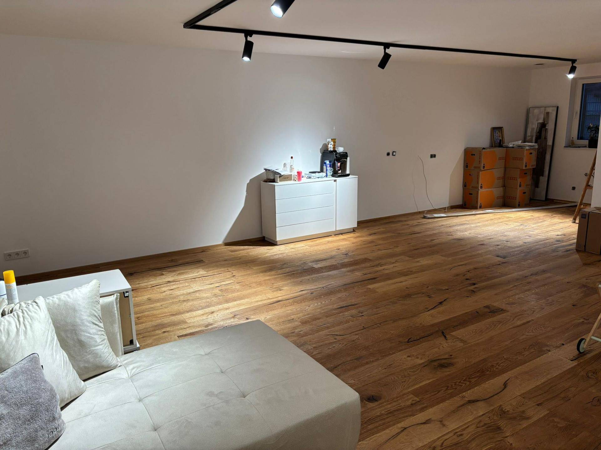 Großzügiges Wohnzimmer mit Holzboden, moderner Beleuchtung und viel Platz.