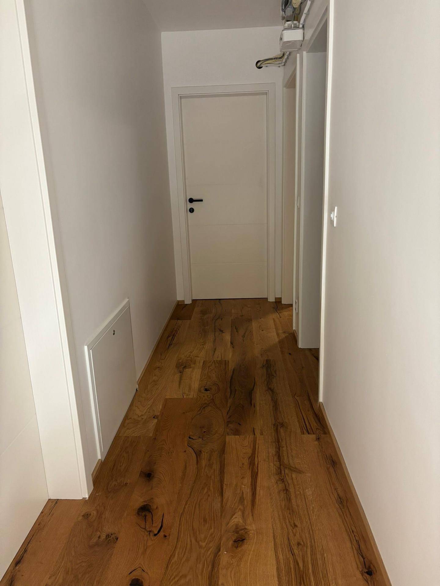 Heller Flur mit Holzboden und weiß gestrichenen Wänden, der zu weiteren Räumen führt.