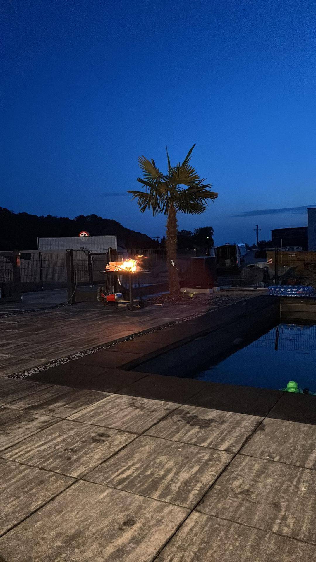 Beleuchteter Poolbereich mit Palmen und Feuerstelle in der Abenddämmerung.