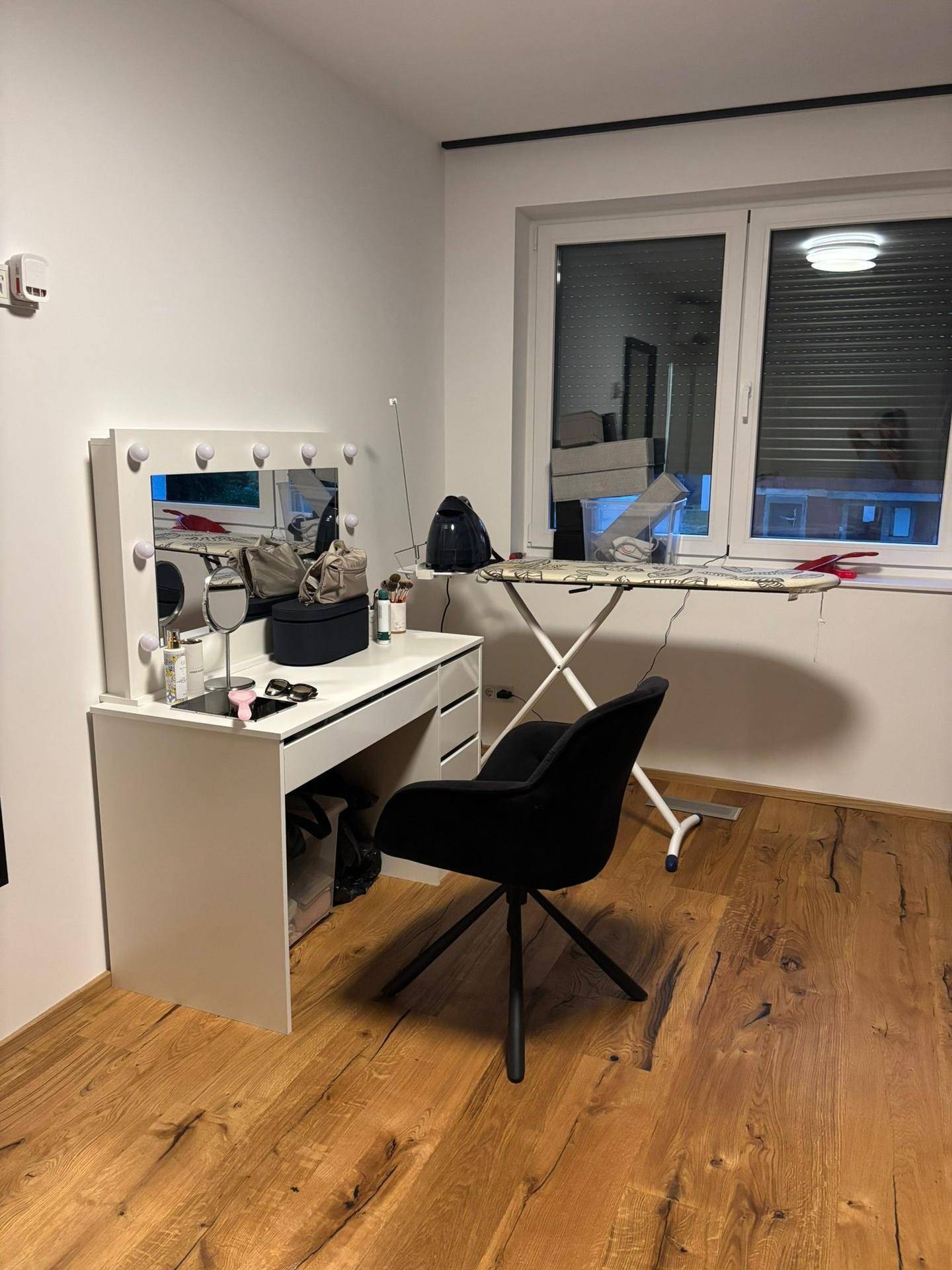 Schlafzimmer mit modernem Schminktisch, beleuchtetem Spiegel und Holzboden.