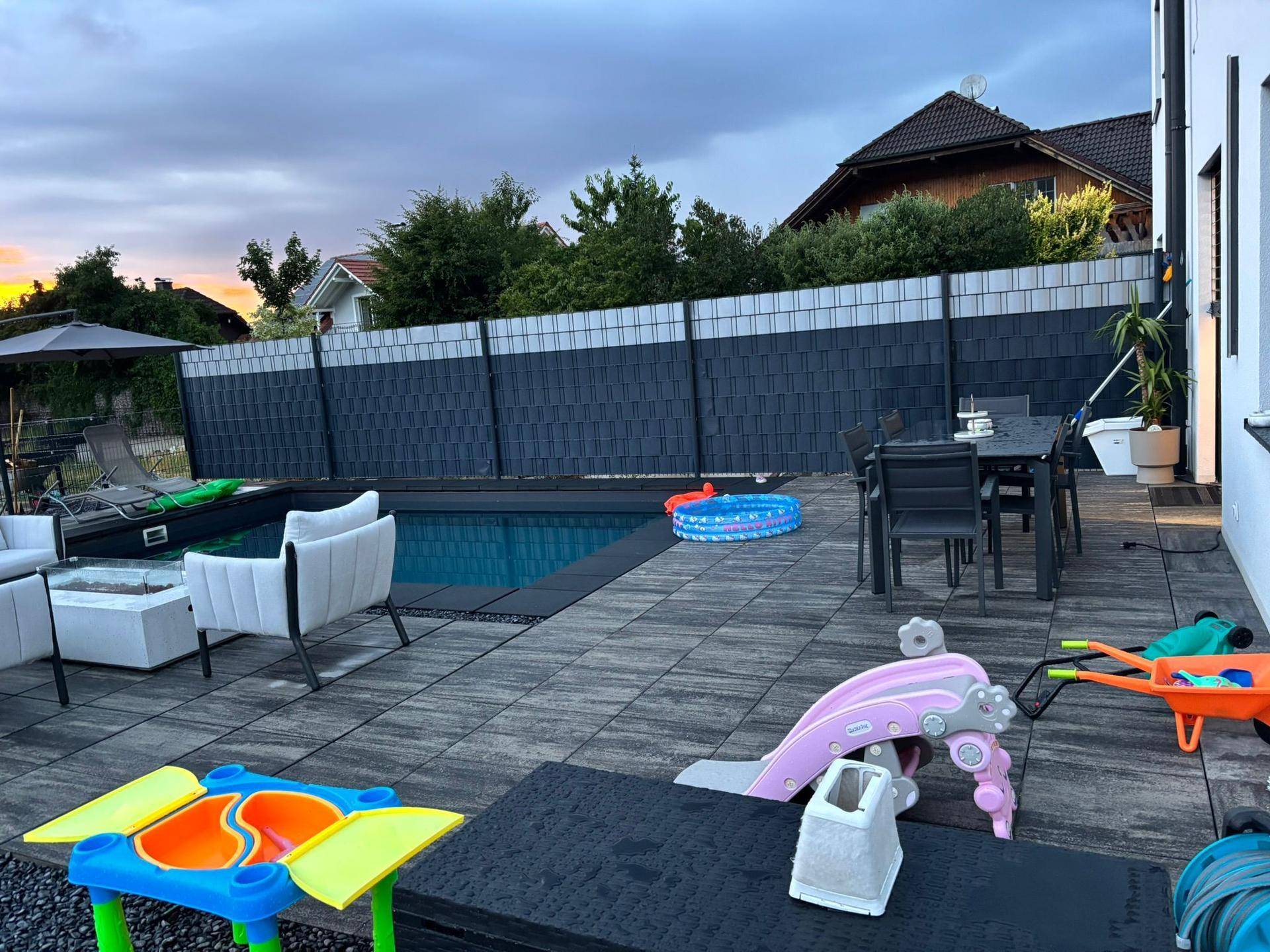 Geräumige Terrasse mit Pool, Lounge-Möbeln und Kinderspielzeug im Freien.