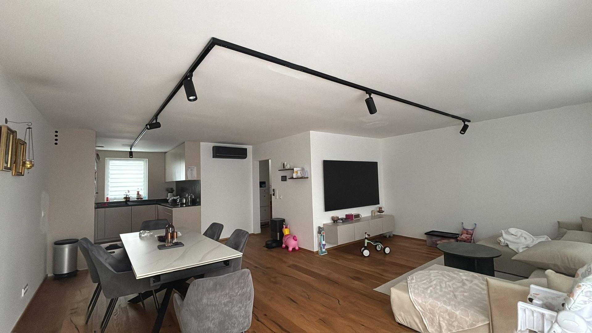 Offener Wohn-Essbereich mit integrierter Küche, Holzboden und moderner Beleuchtung.