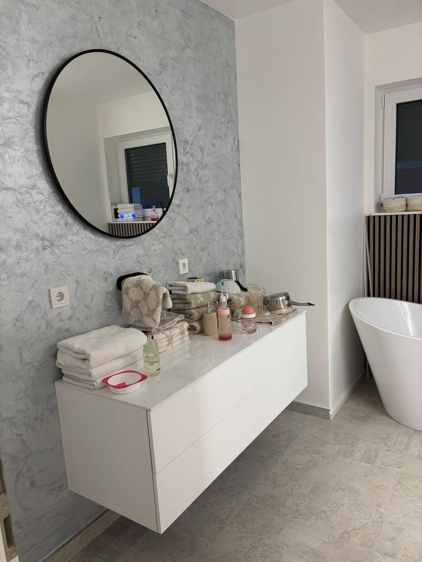 Modernes Badezimmer mit schwebendem Waschtisch, rundem Spiegel und strukturierter Wand.