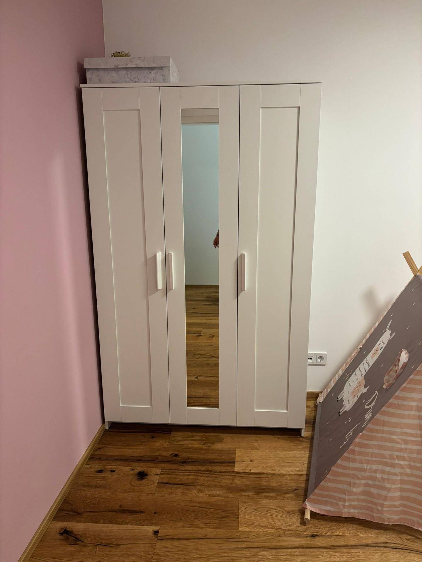 Kinderzimmer mit weißem Kleiderschrank, Spiegel und Holzboden.