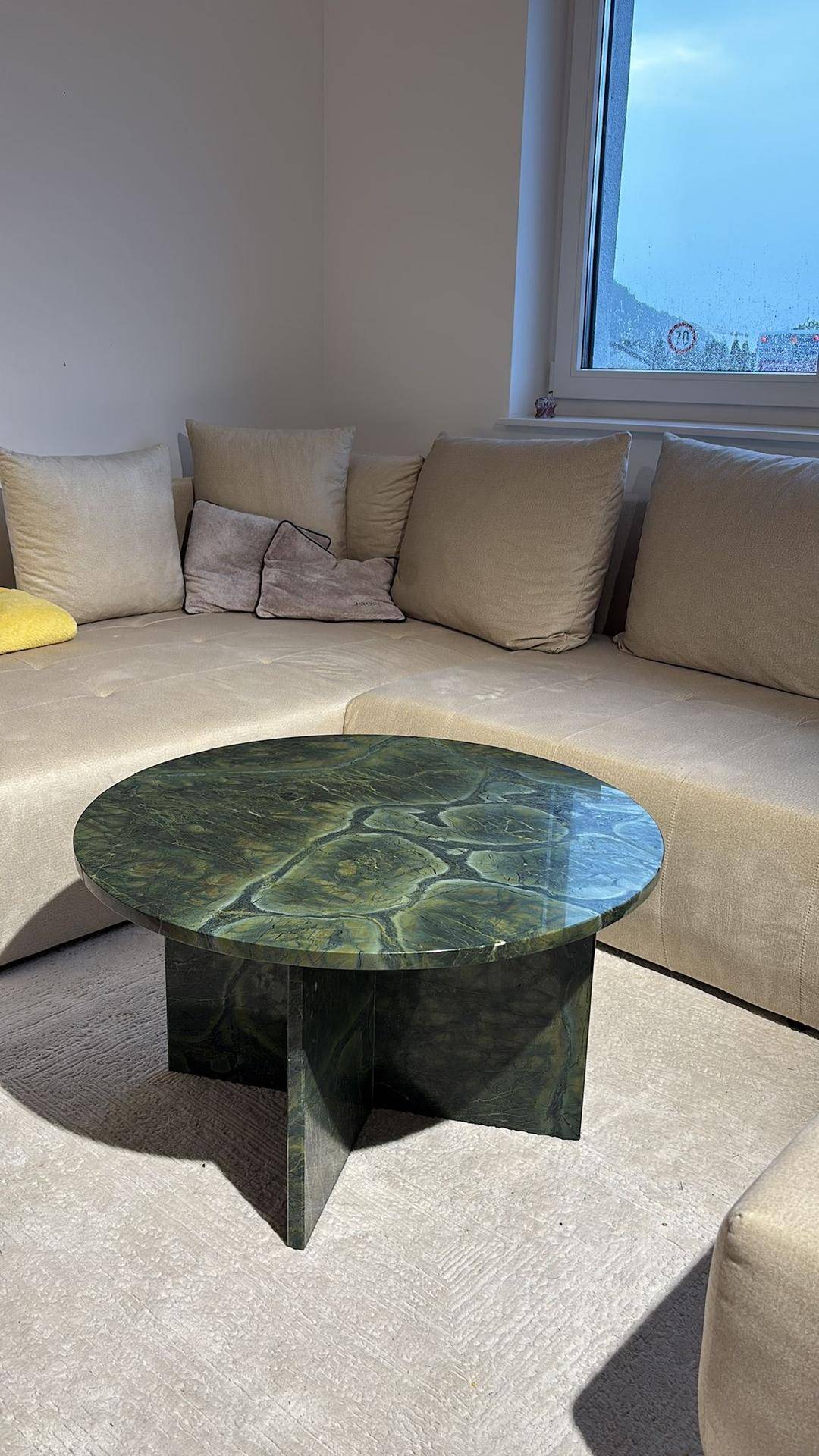 Wohnzimmer mit beigem Sofa und auffälligem grünen Couchtisch aus Naturstein.