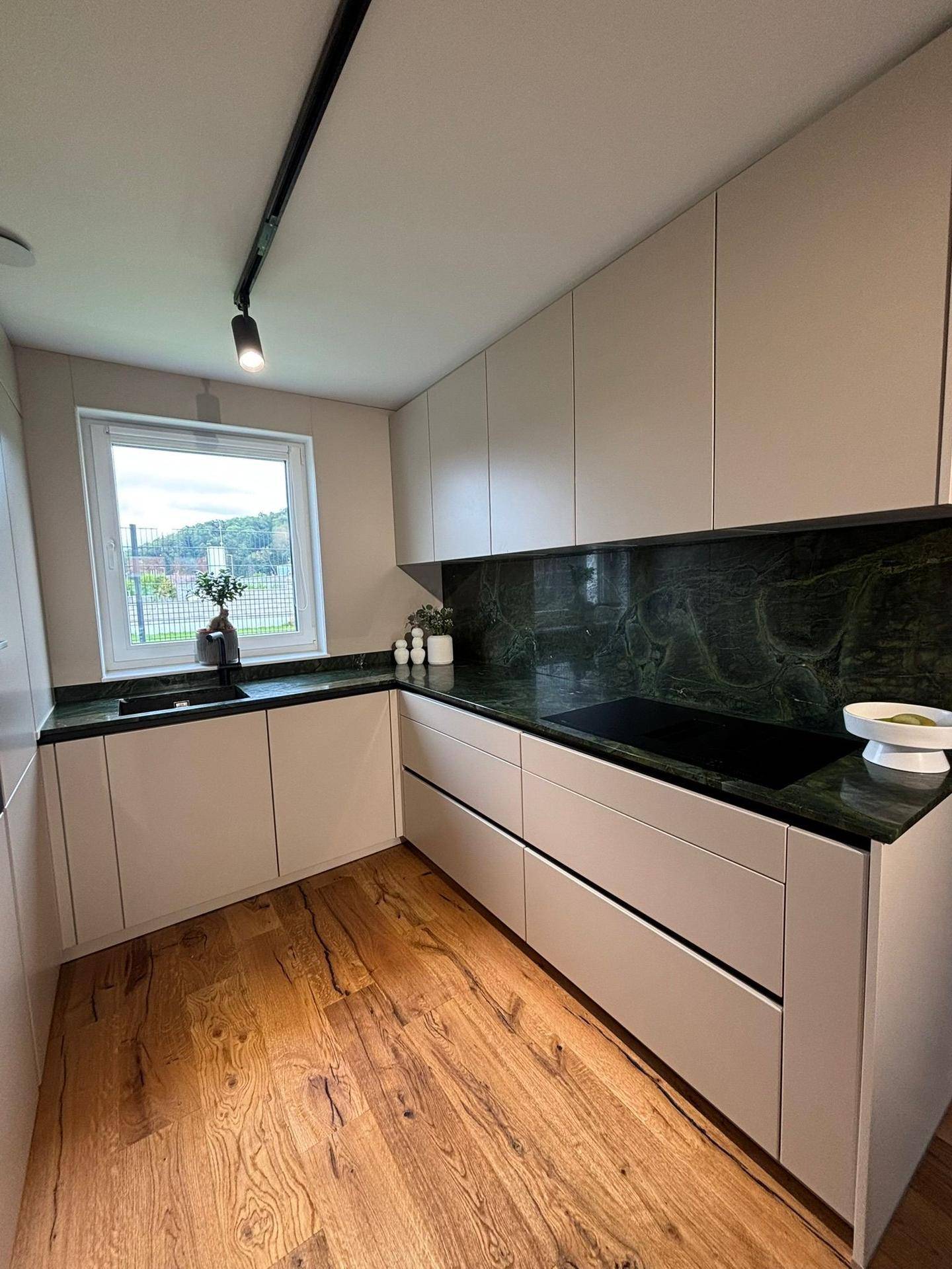 Moderne Küche mit hellen Schränken, dunklen Arbeitsplatten und Fenster mit Ausblick.