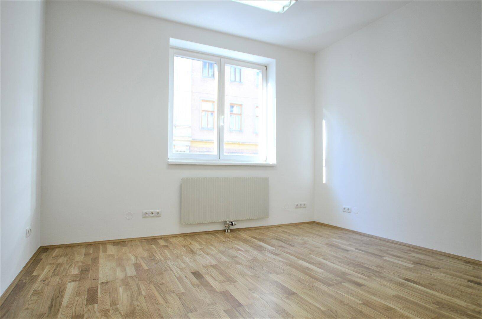 Heller Büroraum mit Holzboden und einem großen Fenster, das viel natürliches Licht spendet.