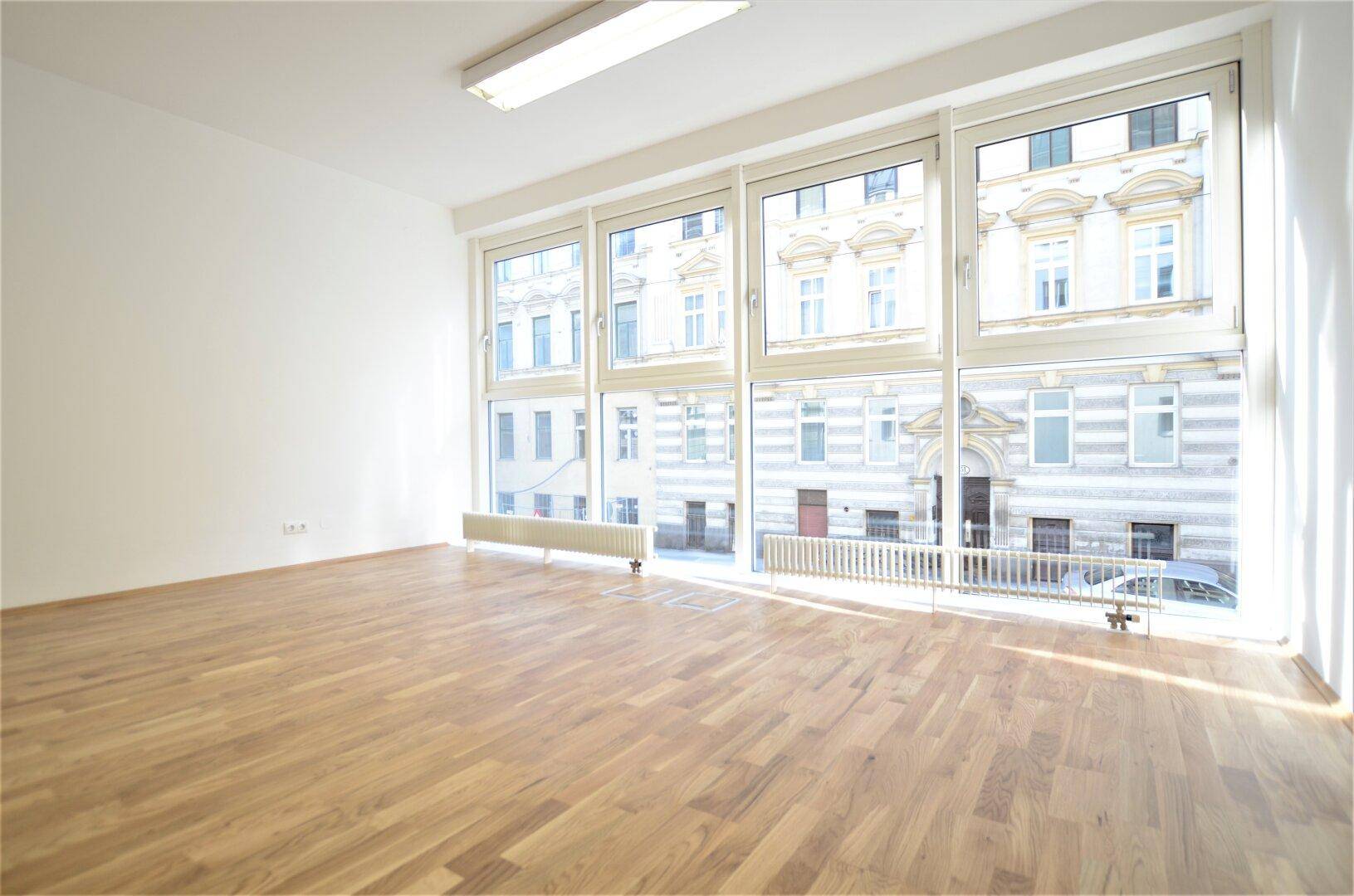 Geräumiger Büroraum mit großen Fenstern und Blick auf die Stadt, ausgestattet mit Holzboden.