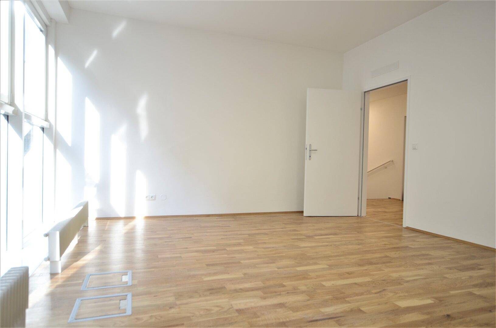 Geräumiger Büroraum mit Holzboden und großen Fenstern, die viel Sonnenlicht hereinlassen.