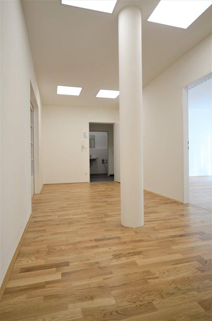 Heller Flur mit Holzboden und einer zentralen Säule, der zu einem Badezimmer führt.