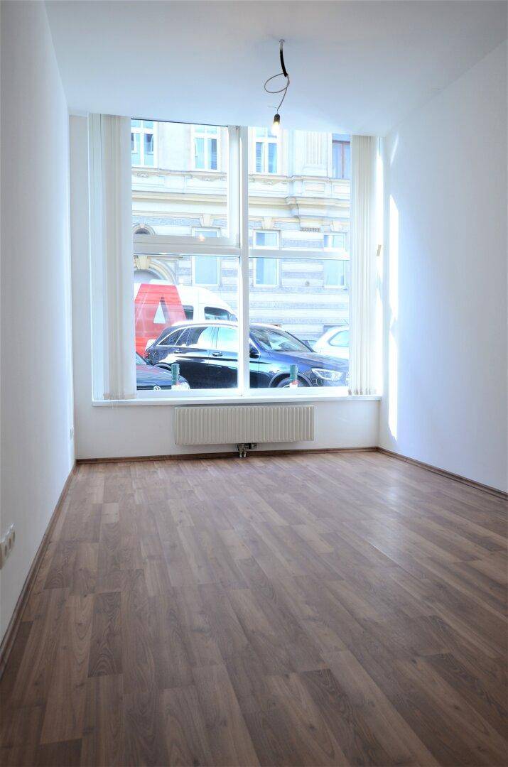 Heller Büroraum mit Laminatboden und großem Fenster zur Straße, ideal für Arbeitsbereiche.