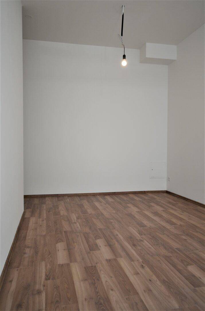Leerer Büroraum mit Laminatboden und weißen Wänden, bereit zur individuellen Gestaltung.
