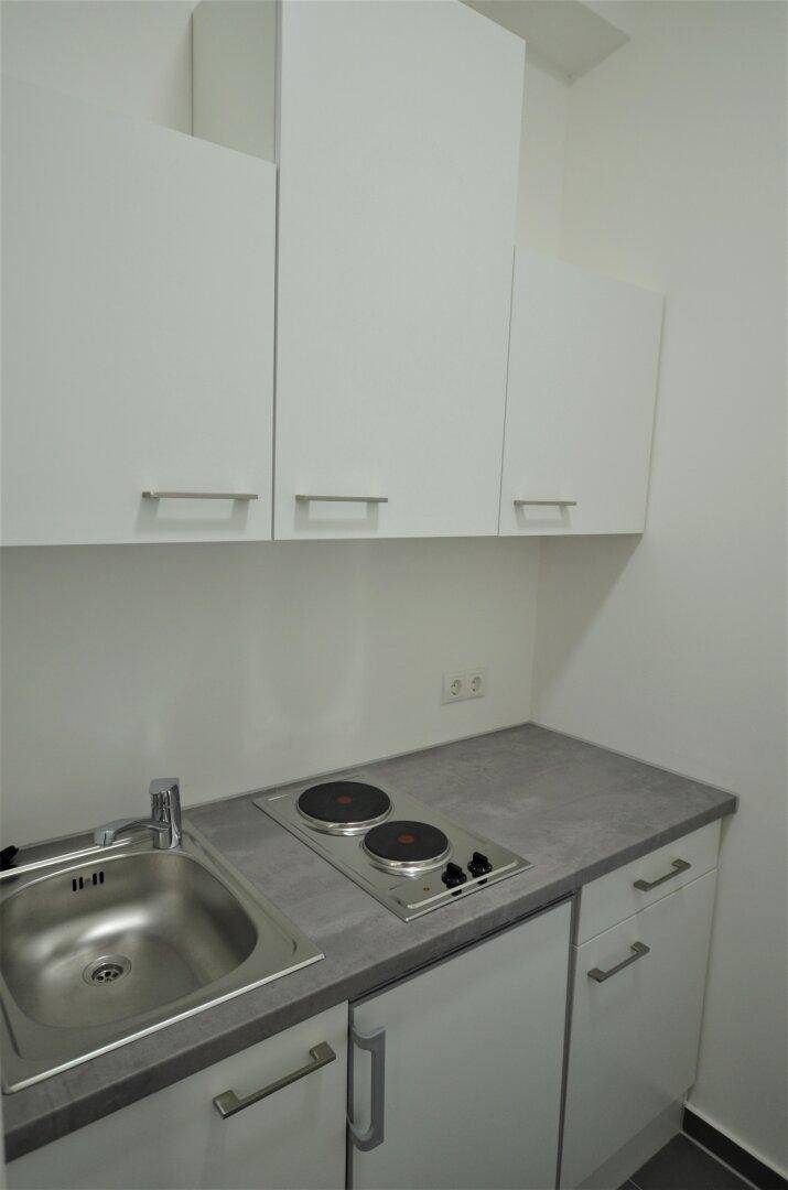 Kleine Küchenzeile mit weißen Schränken, Spüle und zwei Kochplatten, ideal für Büro oder Apartment.