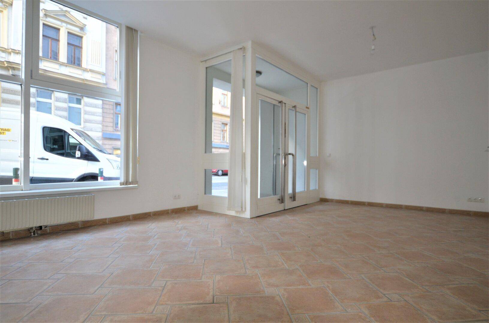 Ladenfläche mit Terrakotta-Fliesenboden und großen Schaufenstern zur Straße hin.