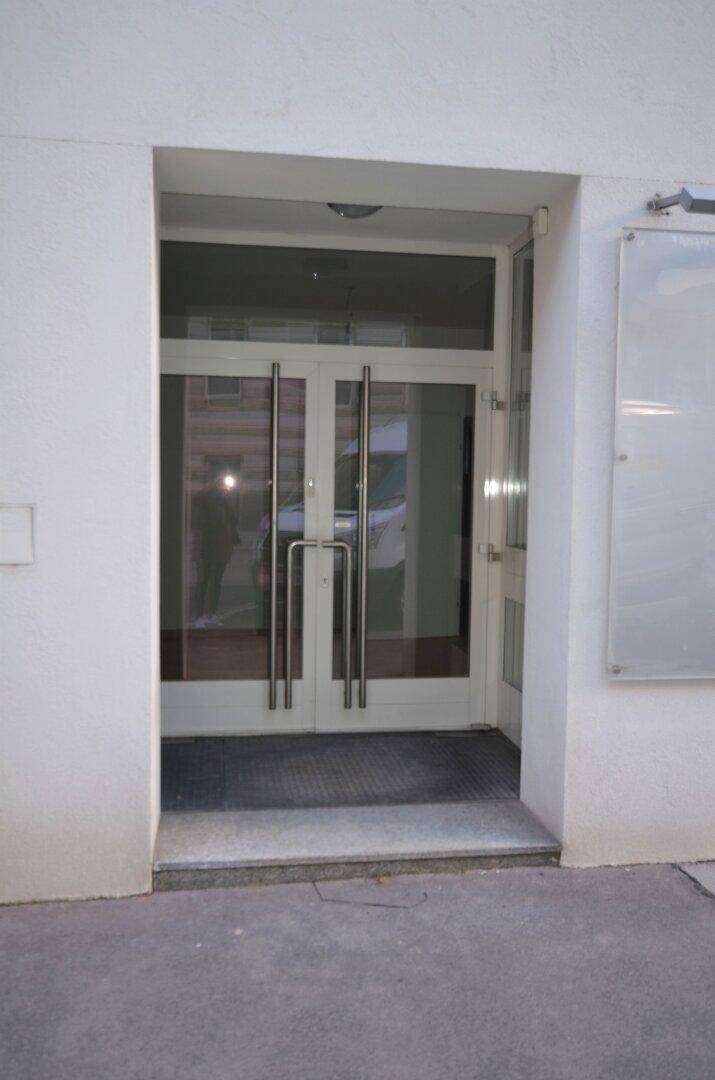 Eingangsbereich eines Gebäudes mit modernen Glastüren und Stufen, die zur Straße führen.