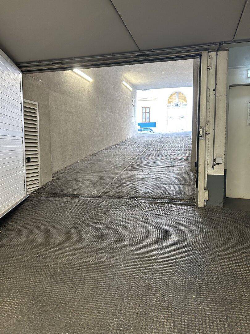 Ausfahrt einer Tiefgarage mit Rampe, die ins Freie und zu einem historischen Gebäude führt.