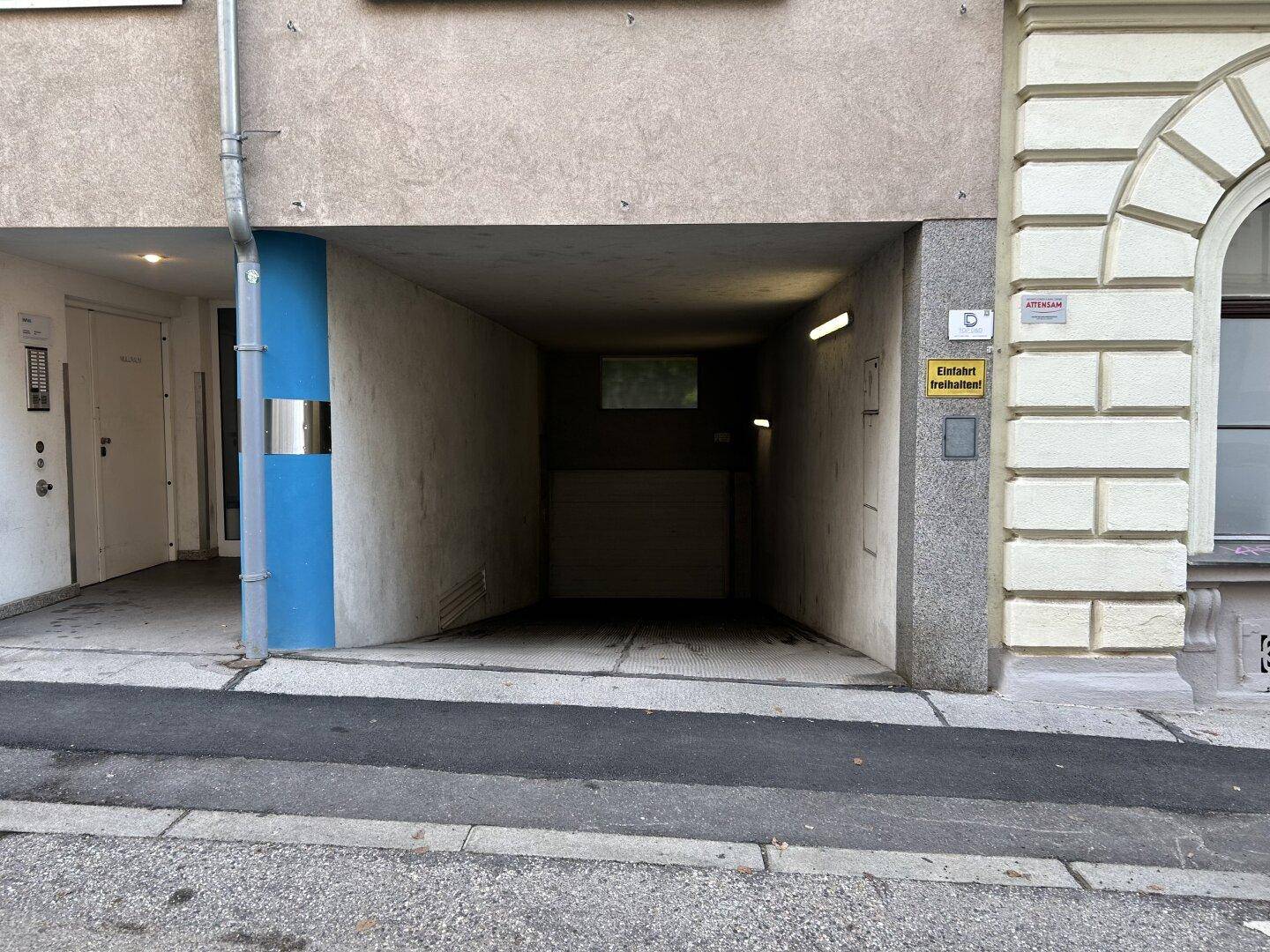 Einfahrt zur Tiefgarage von der Straße aus gesehen, mit Hinweisschild und moderner Architektur.