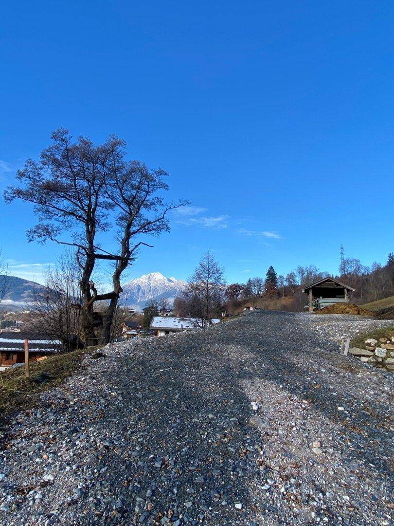 Schotterweg führt zu einem Aussichtspunkt mit Blick auf einen schneebedeckten Berg und umliegende Häuser.