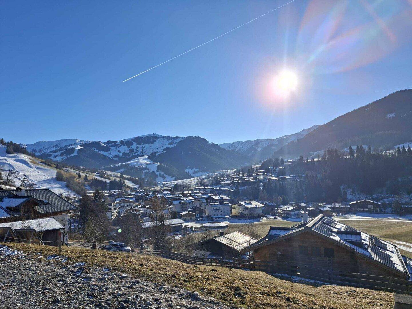 Panoramablick auf ein verschneites Dorf in einem Tal, umgeben von Bergen unter strahlendem Sonnenschein.