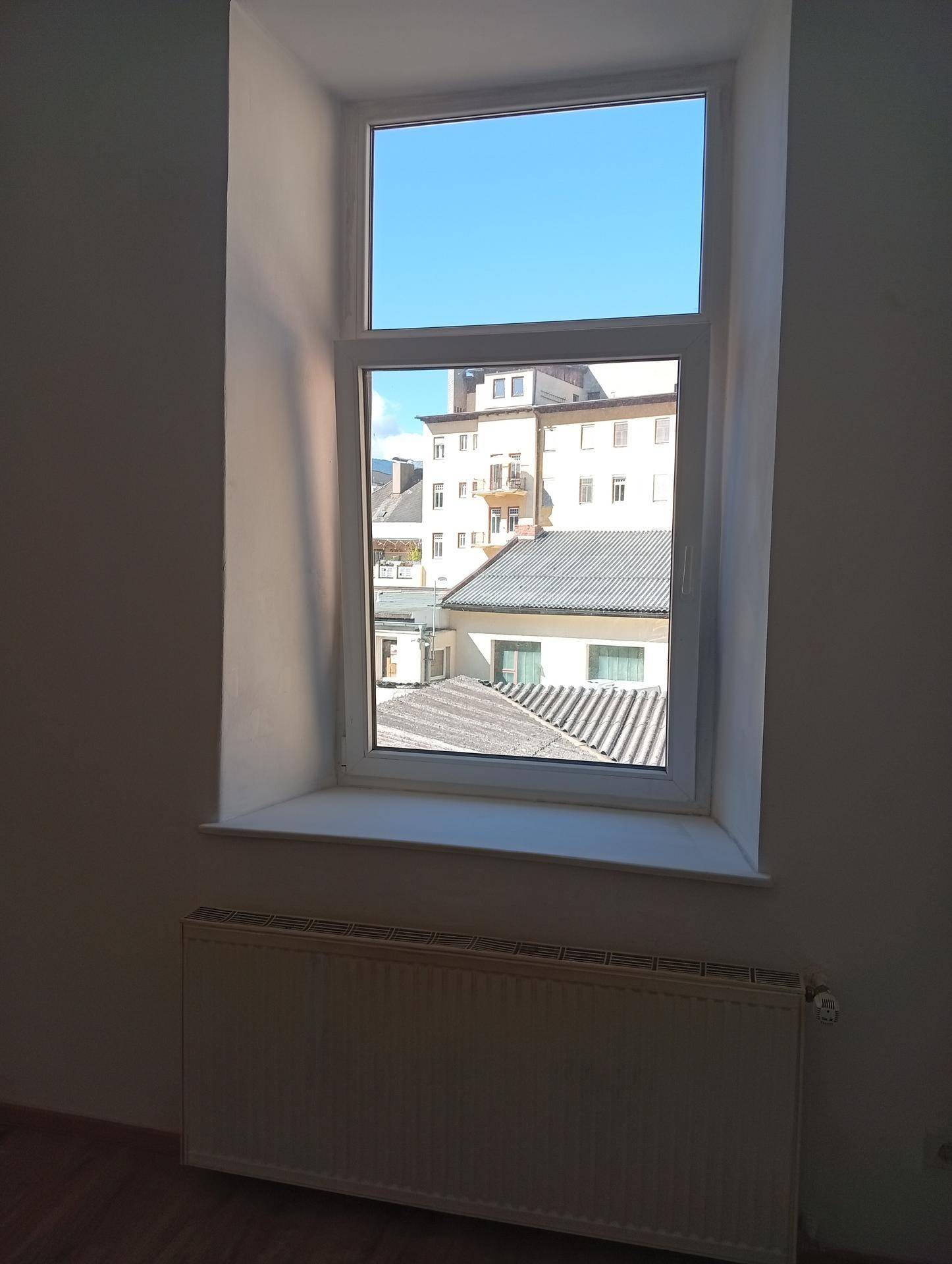 Fenster in einem leeren Raum mit Blick auf die umliegenden Gebäude und den blauen Himmel.