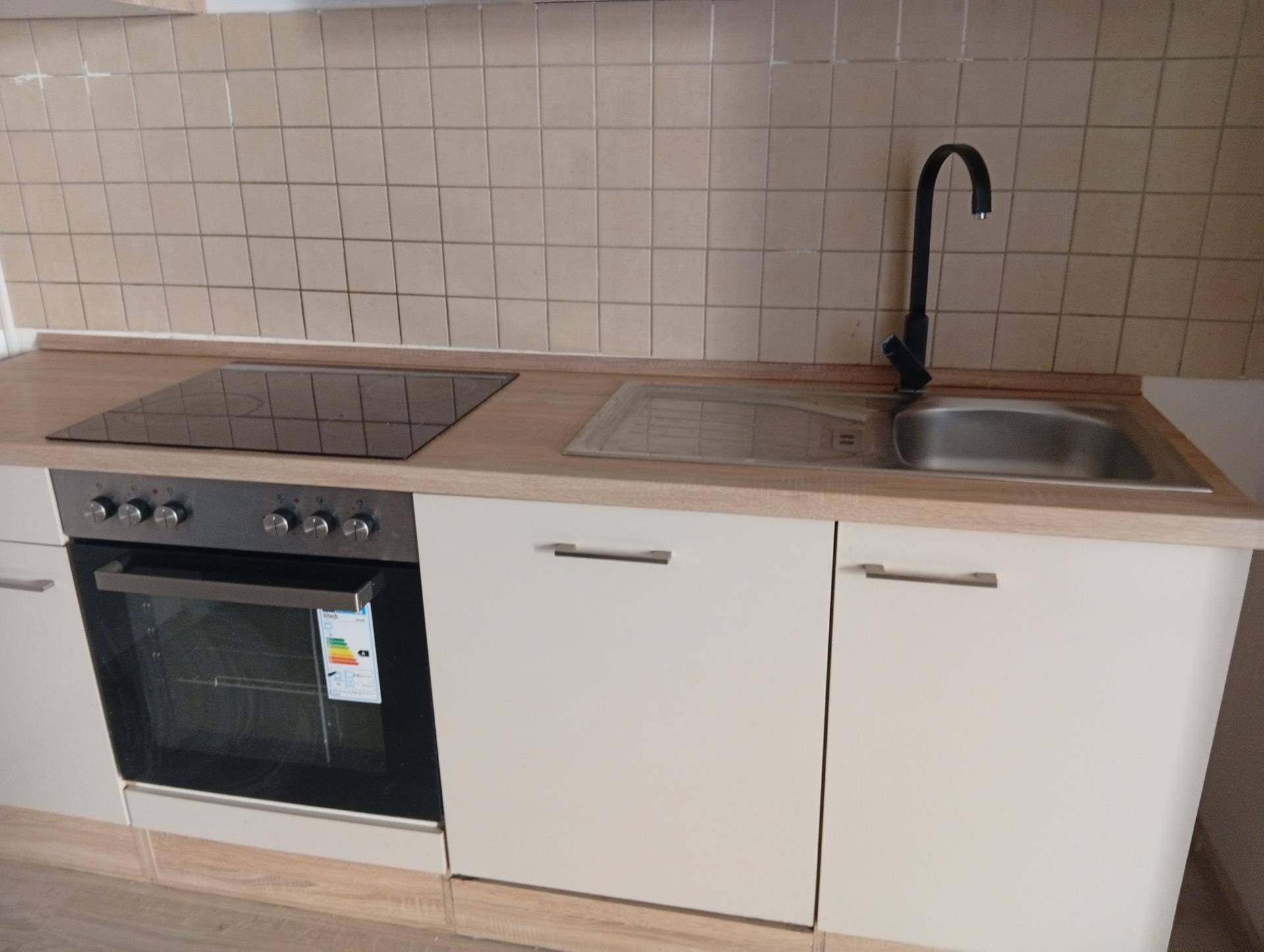 Moderne Küchenzeile mit Induktionskochfeld, Backofen, Spüle und hellen Holz-Arbeitsplatten.