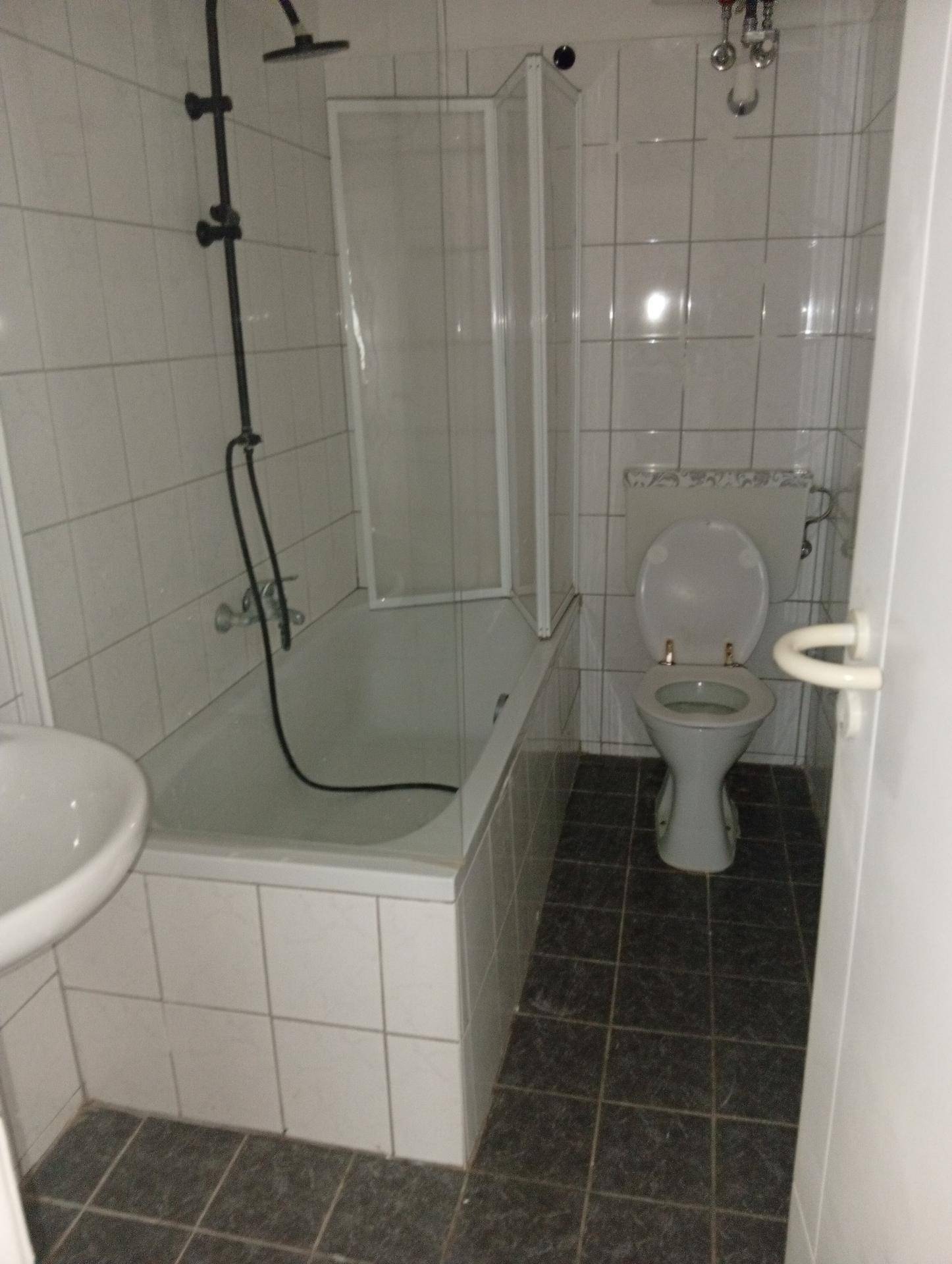 Badezimmer mit Badewanne, Duschvorrichtung, Toilette und weißen Fliesen an den Wänden.