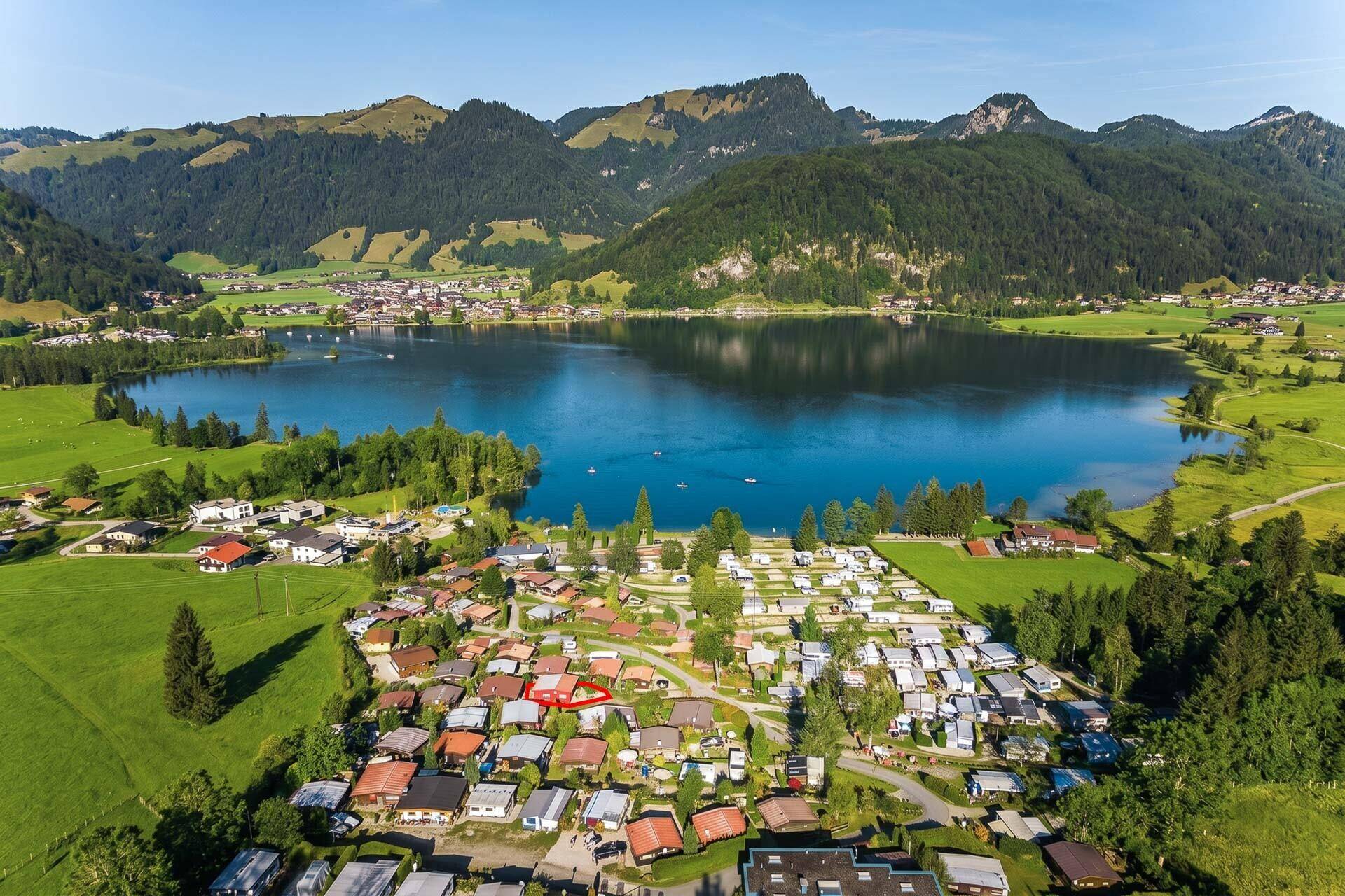Weitläufige Luftaufnahme der Ferienhaussiedlung am See mit beeindruckender Bergkulisse.