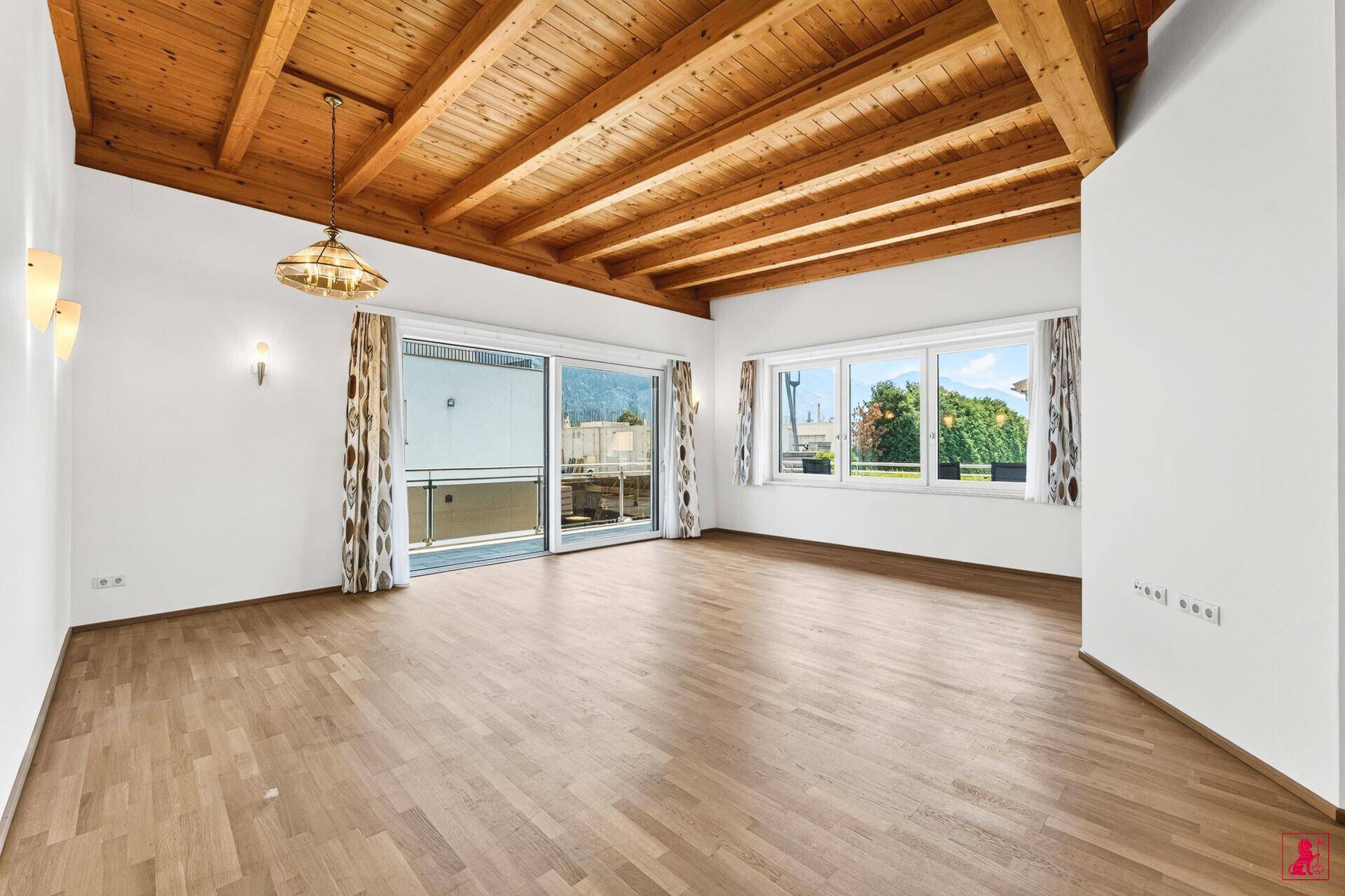 Geräumiges Wohnzimmer mit Holzbalkendecke, Parkettboden und Zugang zu einem Balkon.