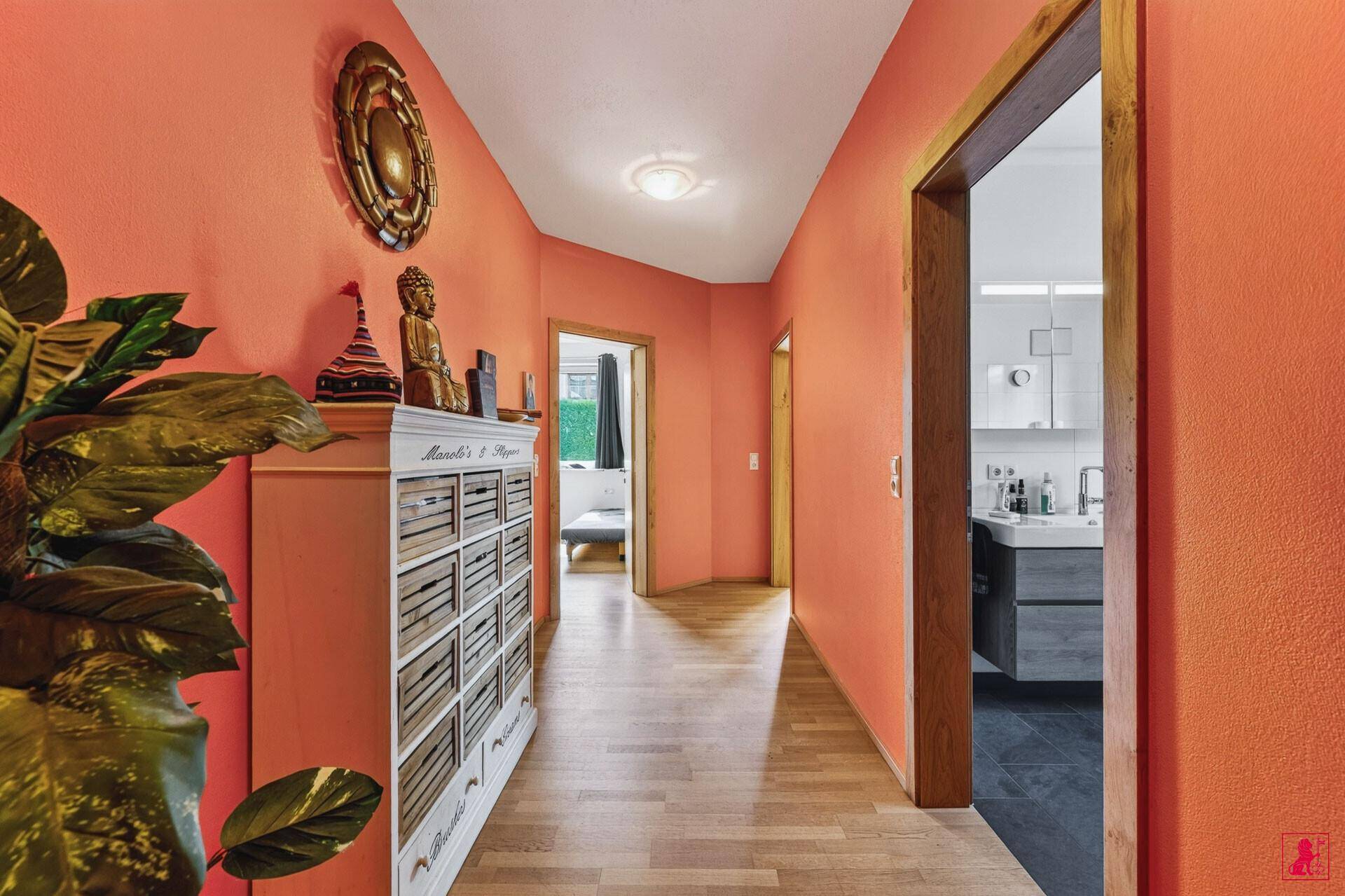 Langer Flur mit orangefarbenen Wänden, Holzboden und Zugang zur Küche.