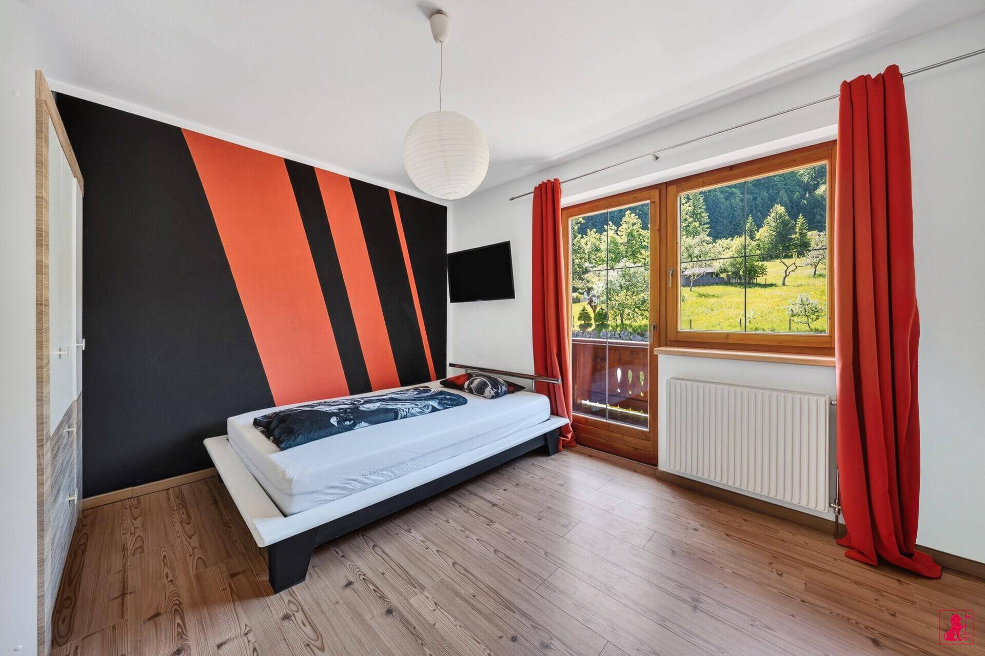 Schlafzimmer mit auffälliger Wandgestaltung, Holzboden und Balkonzugang.