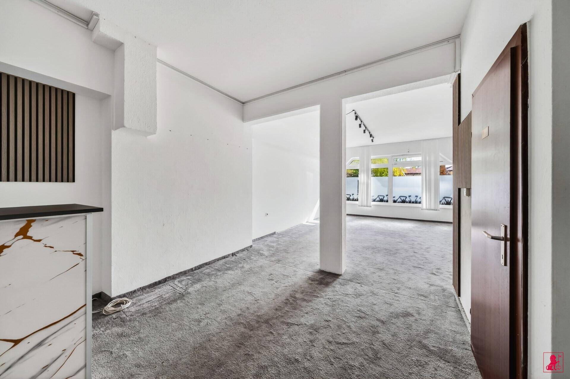Offener Empfangsbereich mit Theke, dunkler Holztür und Blick in einen hellen Raum mit Fenstern.