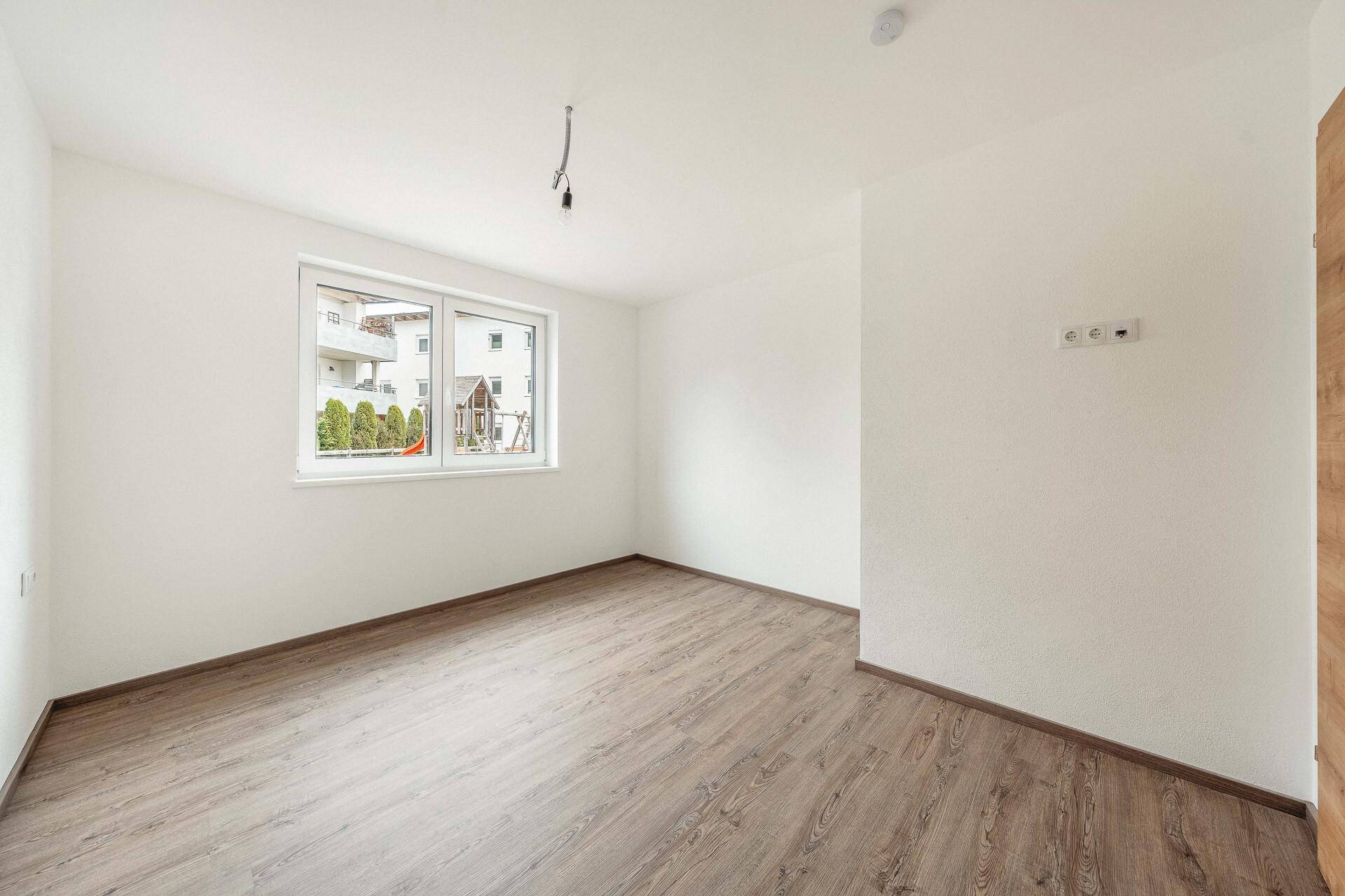 Leeres Zimmer mit modernem Laminatboden und weiß gestrichenen Wänden, bereit zur individuellen Gestaltung.