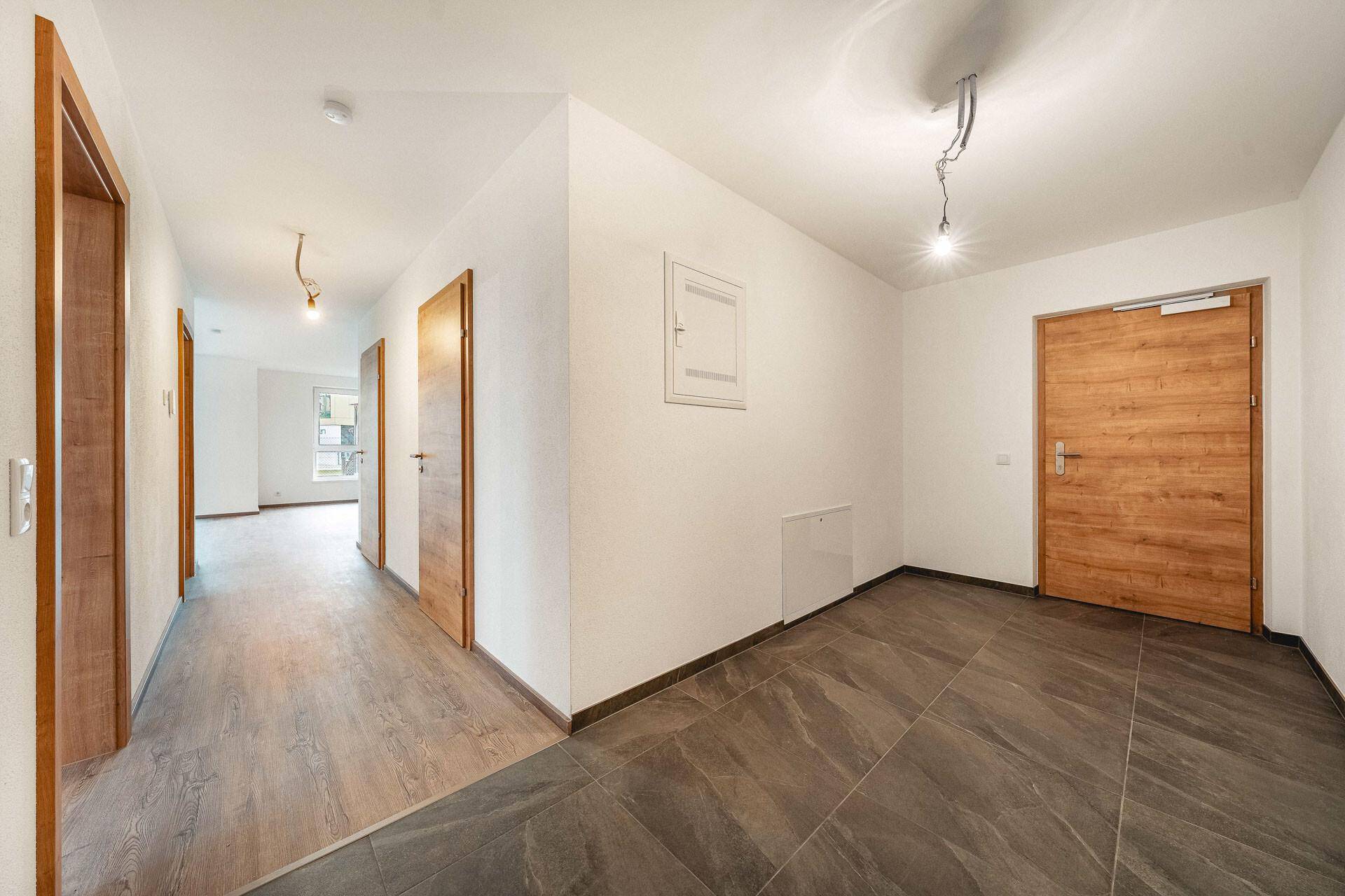 Heller Eingangsbereich mit modernen Fliesen und Holztüren, der zu weiteren Räumen führt.
