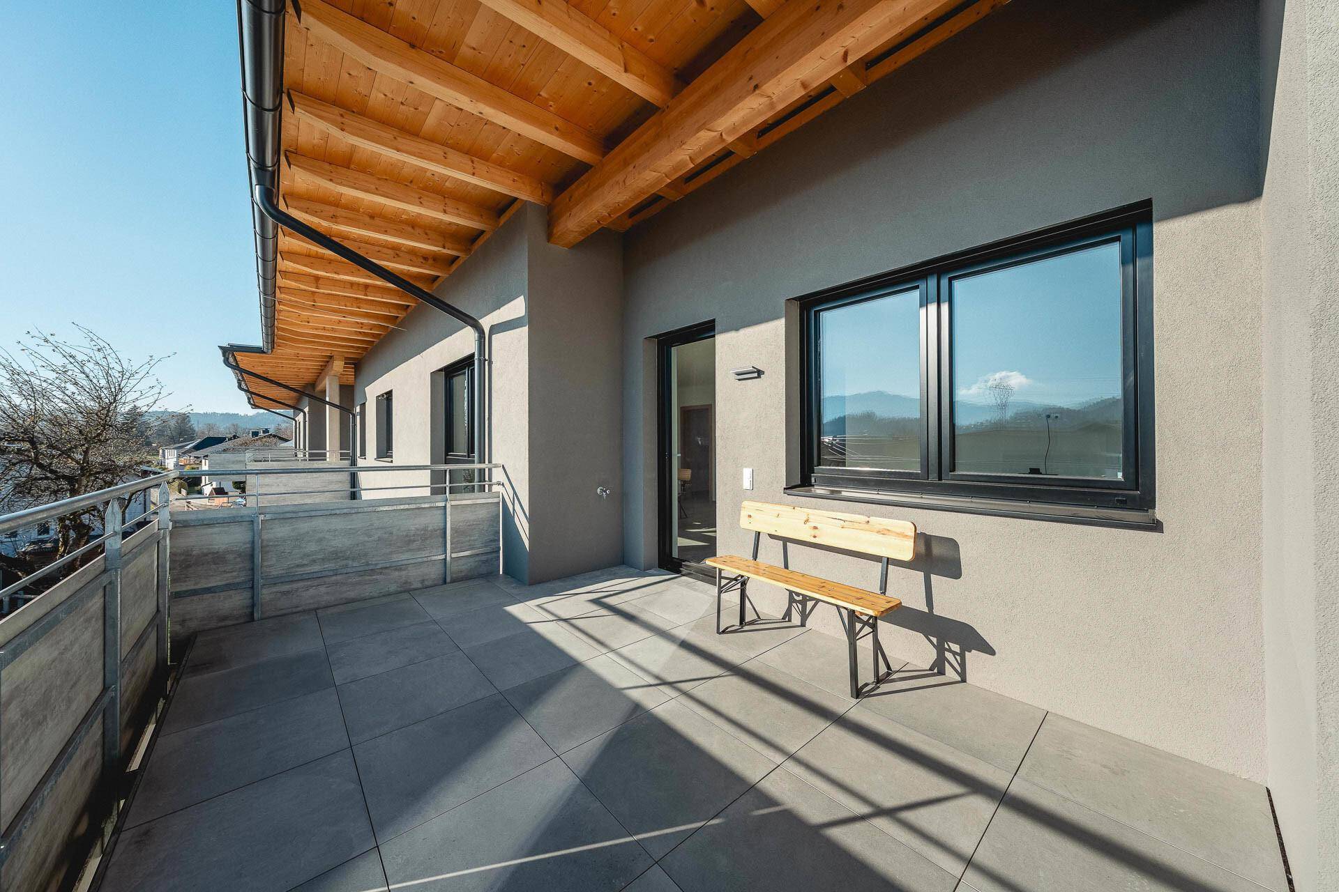 Sonniger Balkon mit Fliesenboden, Holzdach und einer Holzbank, ideal zum Entspannen.