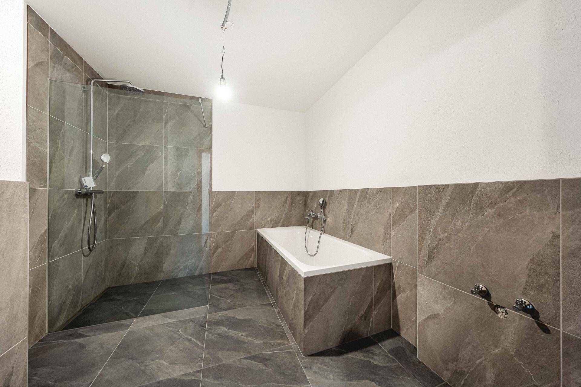 Geräumiges Badezimmer mit Badewanne, begehbarer Dusche und modernen grauen Fliesen.