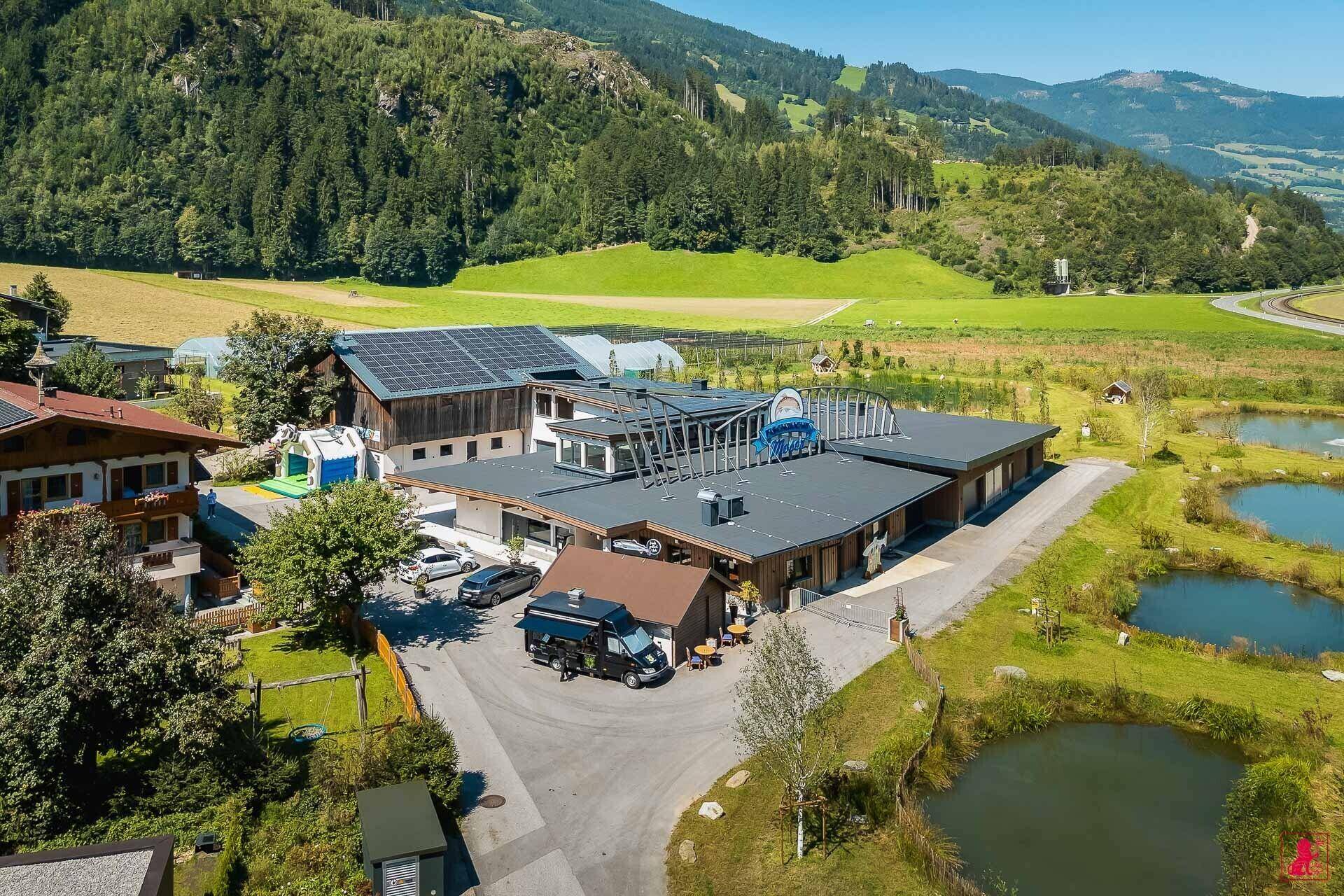Weitläufige Anlage mit mehreren Gebäuden, Teichen und Photovoltaikanlagen, eingebettet in eine Berglandschaft.